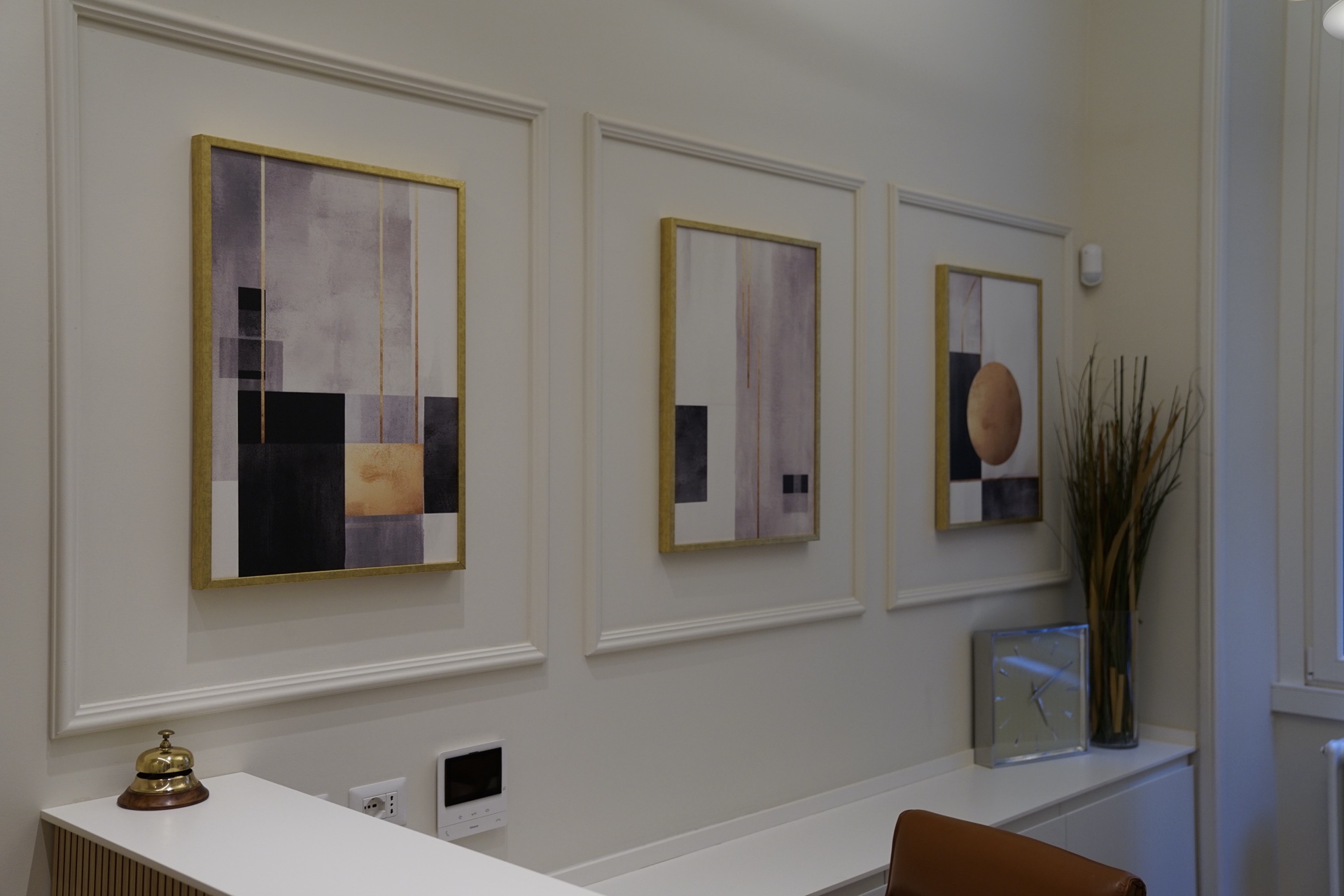 Reception: tre quadri astratti con cornici dorate, bell d'ottone, pianta